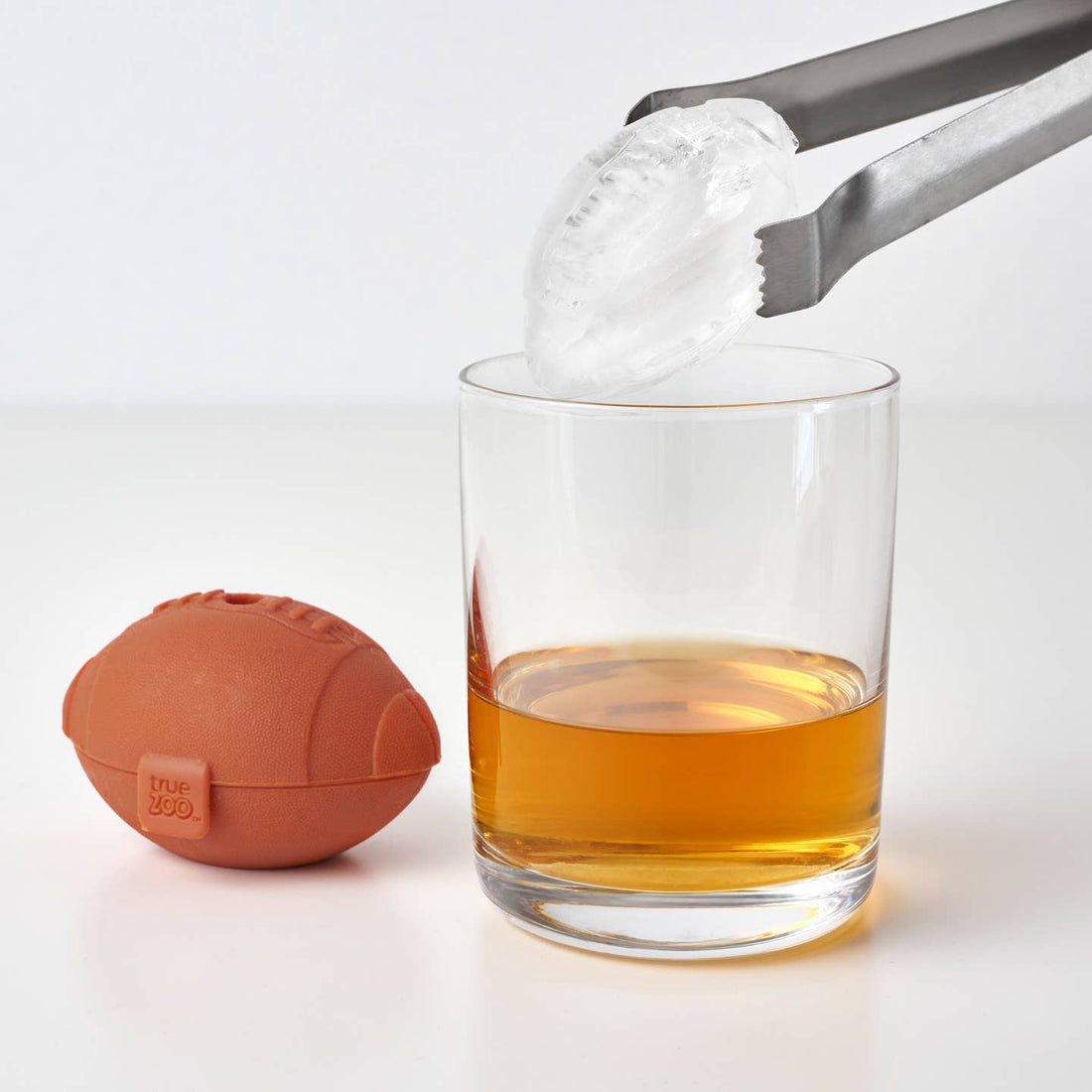 Football-shaped ice cube tray next to a football-shaped ice cube going into a glass of liquid.