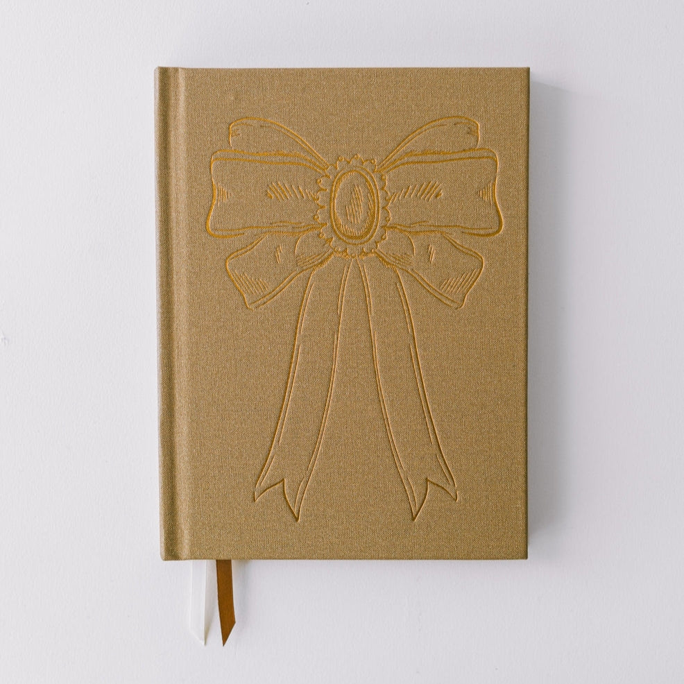 Notebook by Good Juju with gold detailing depicting a bow. 