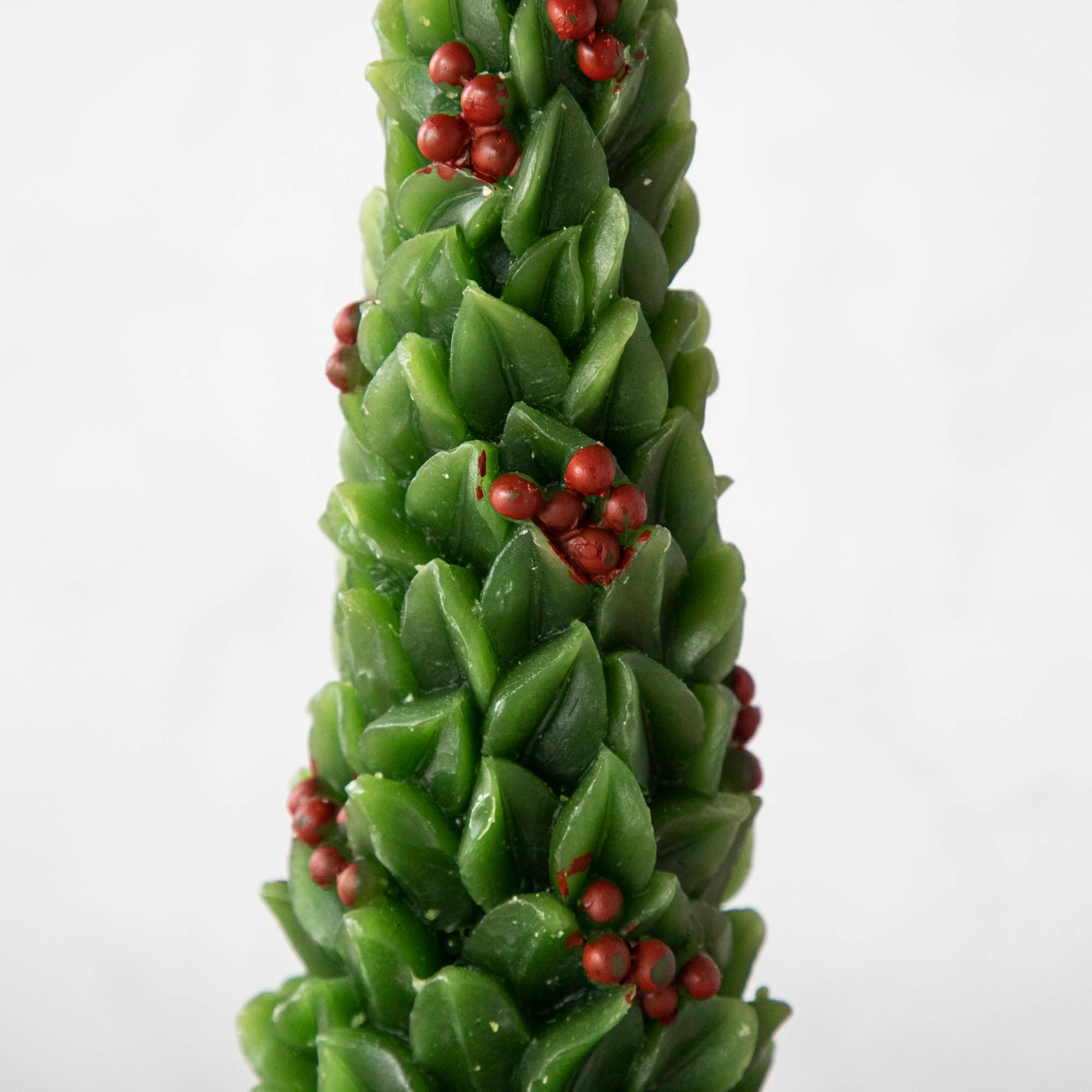 Close-up of a candle designed to resemble a green Christmas trees with red berries.