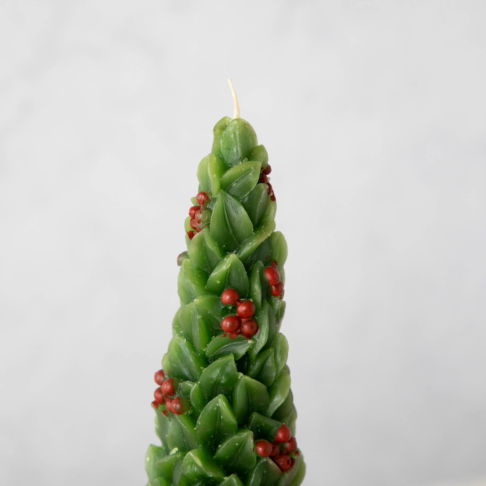 Close-up of a candle designed to resemble a green Christmas trees with red berries.