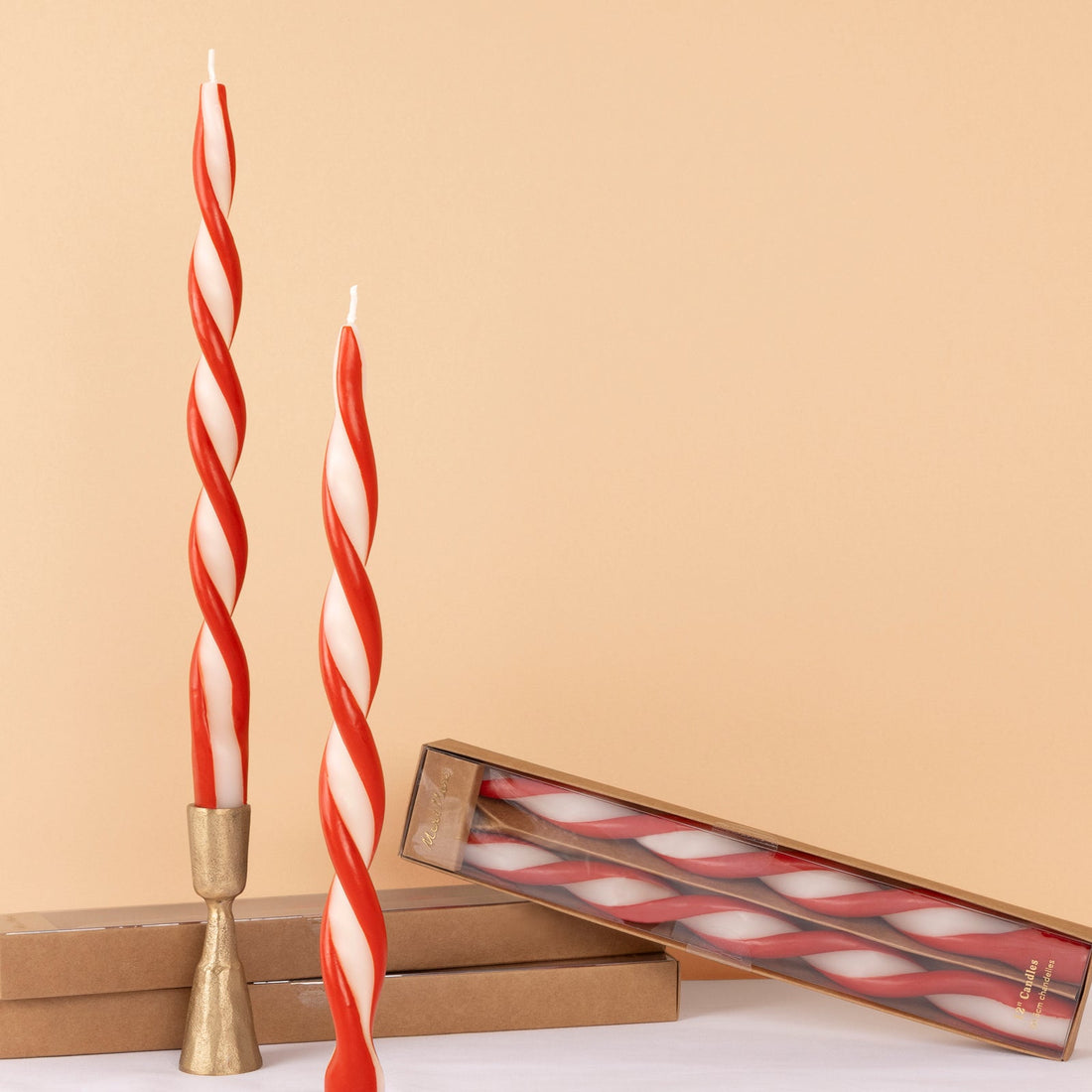 Red and white twisted candles with a gold holder on a beige background.