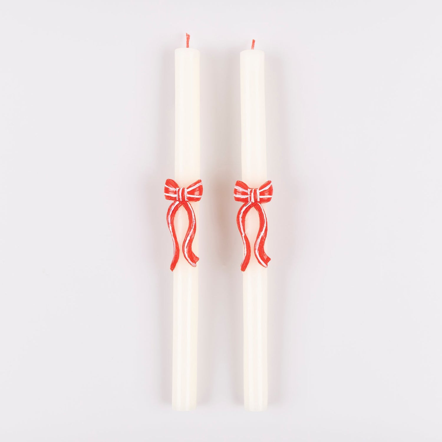 Two white candles with red bow designs on a light gray background