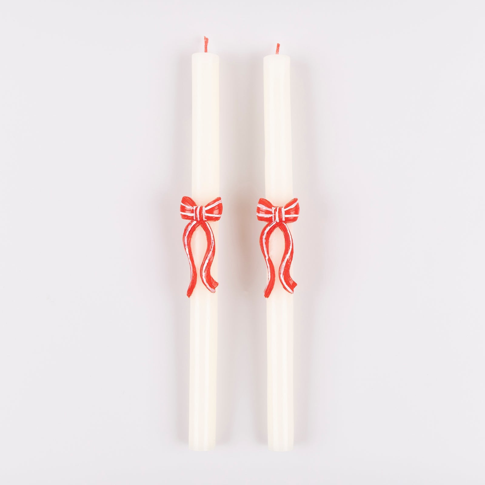 Two white candles with red bow designs on a light gray background
