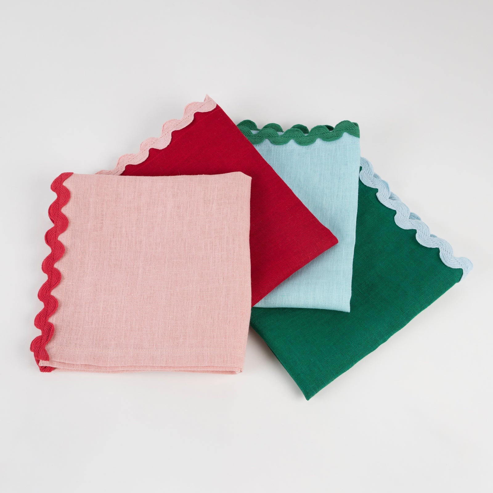 Four colorful napkin squares with scalloped edges on a white background.