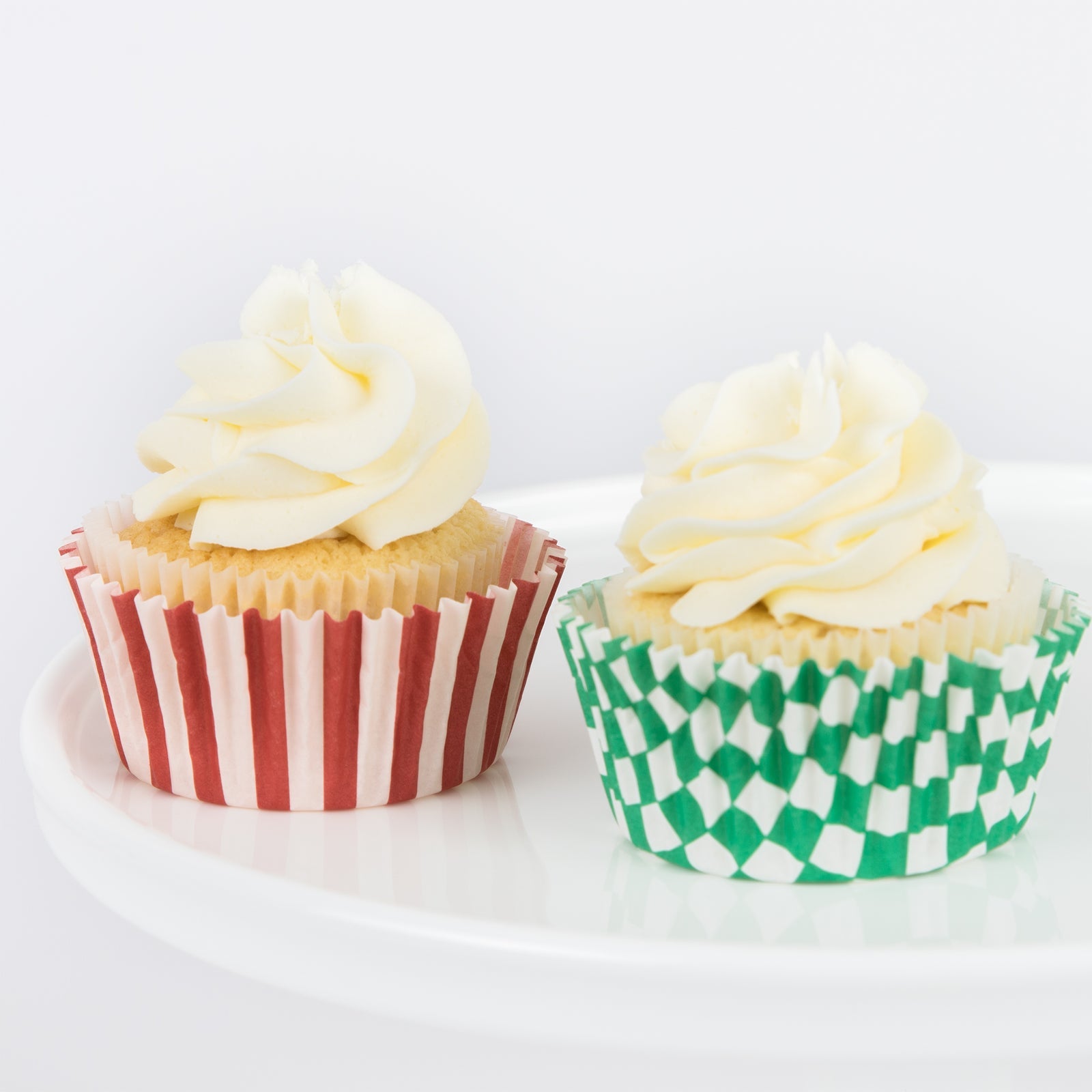 Two cupcakes in festive holiday papers, one red striped one green striped.