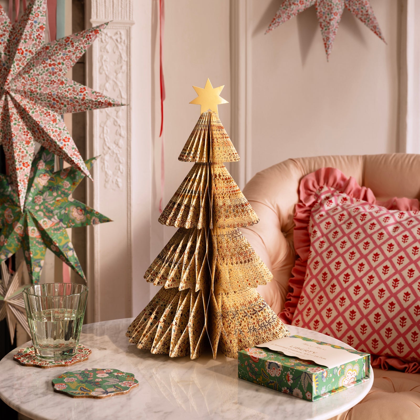 Decorative paper Christmas tree on a table with festive decorations in the background.