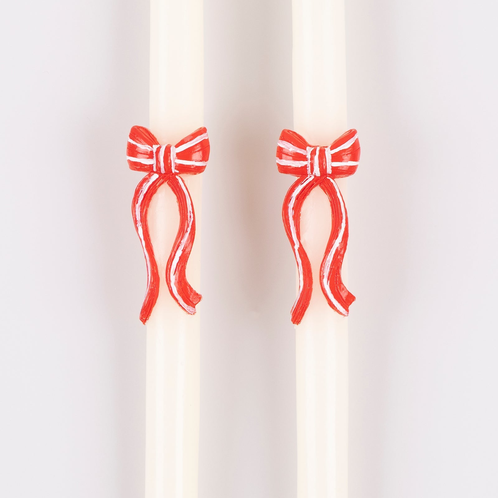 Two candles with red bow decorations on a white background.