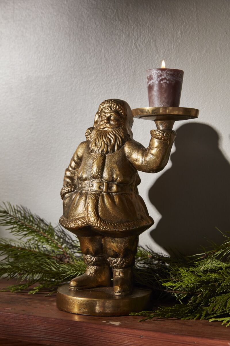 Saint Nick Figurine on a mantle with greenery holding a lit candle.