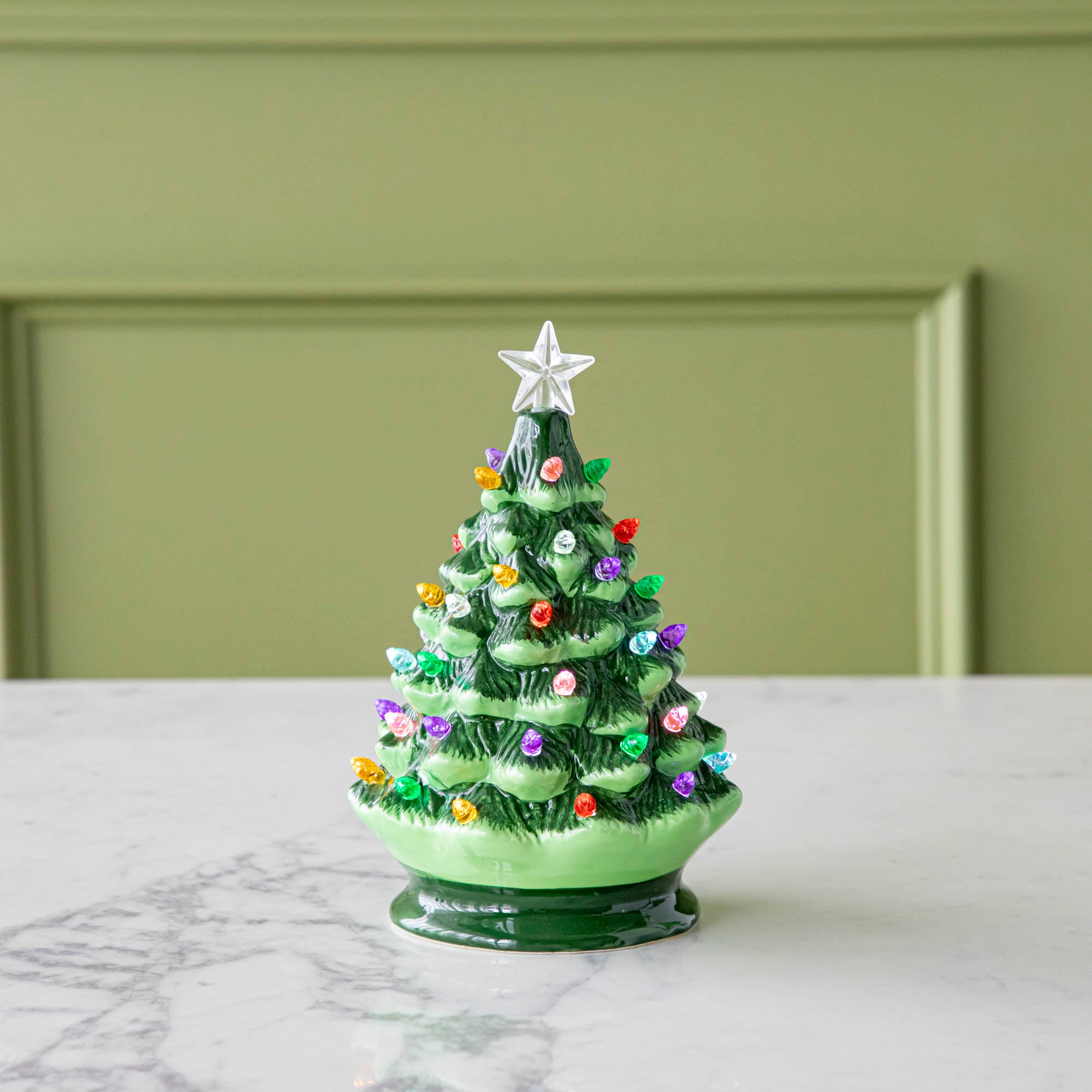 An 8" Porcelain Vintage Lit Tree with Timer on a marble table.