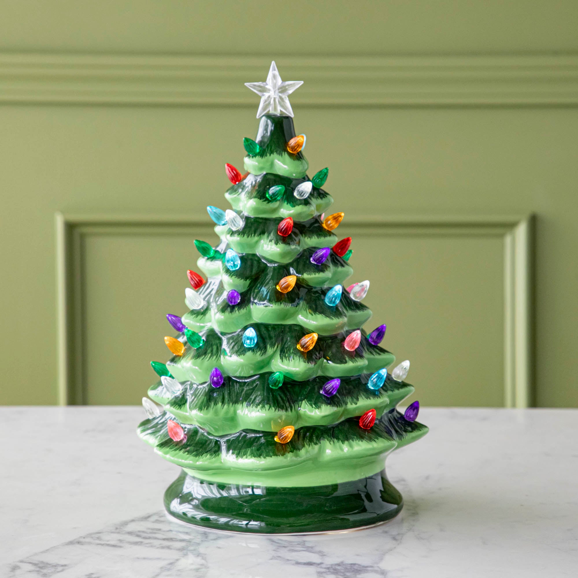 A 13" Porcelain Vintage Lit Tree with Timer on a marble table.