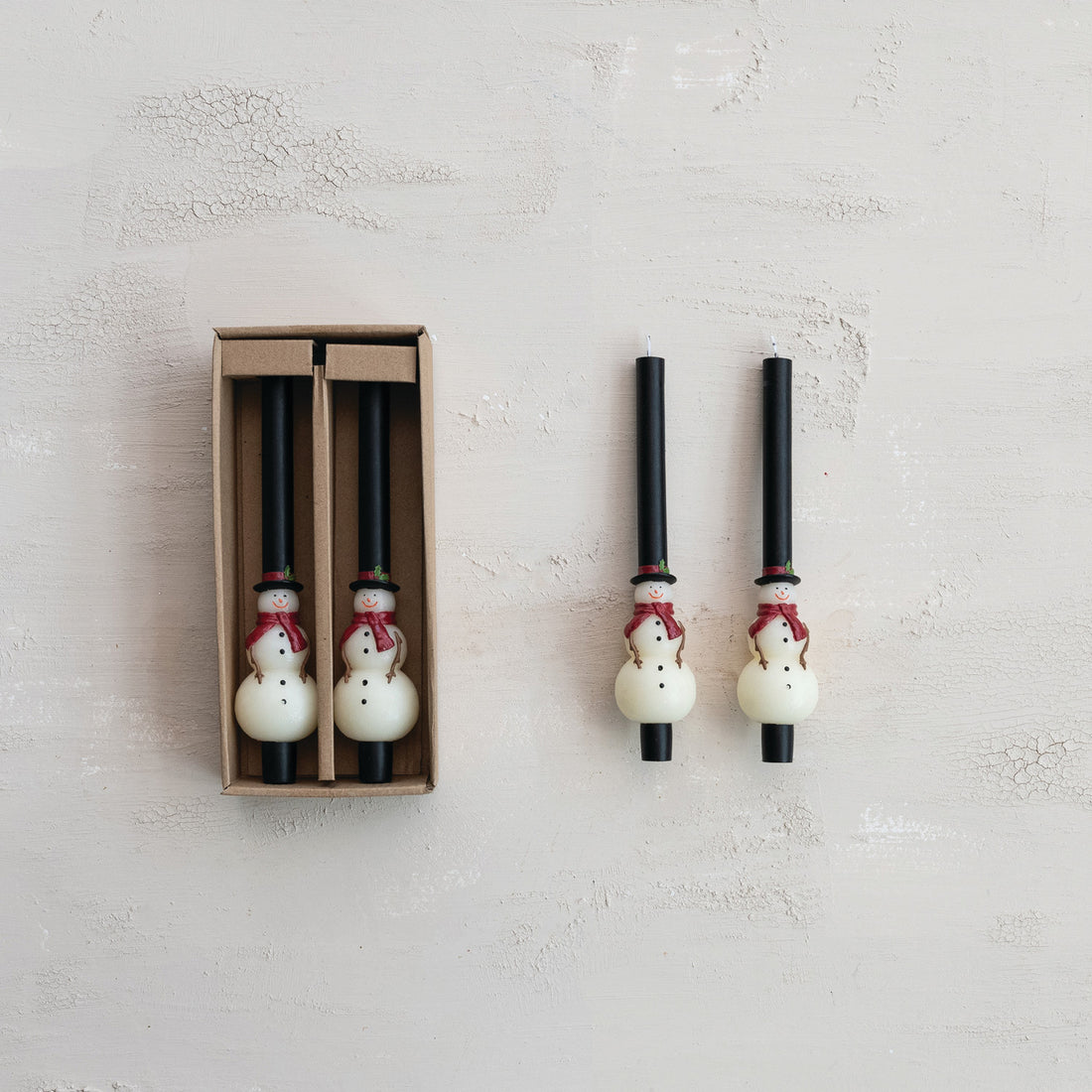Set of snowman-themed candles with one in packaging on a light gray background