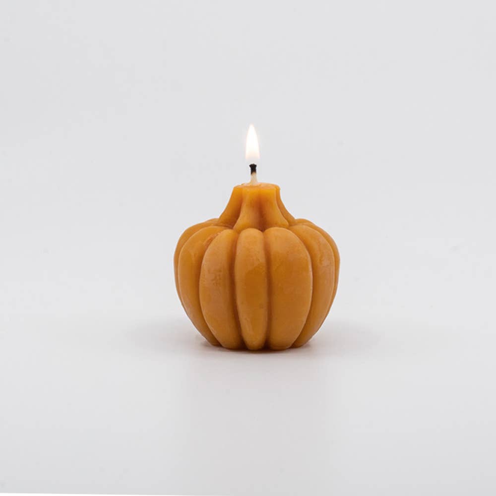 A light orange large pumpkin candle, lit on a white background.