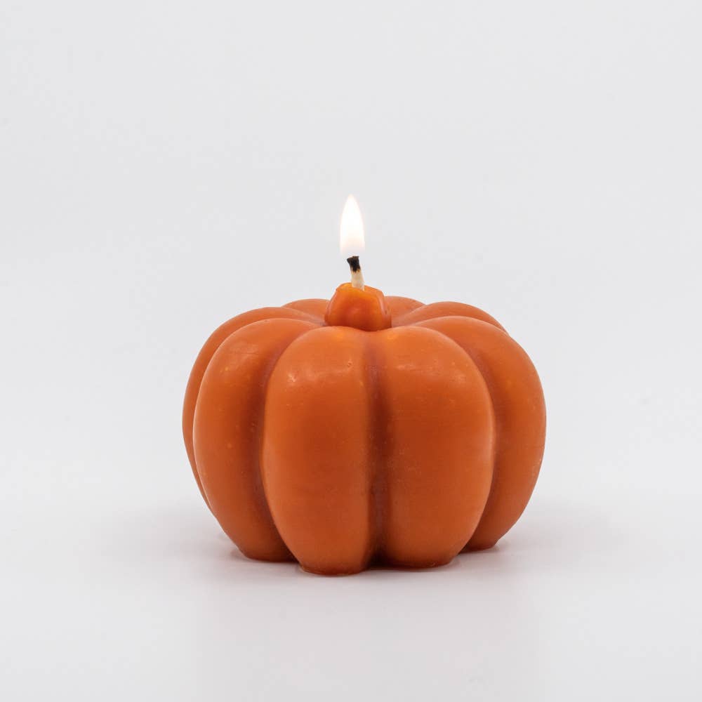 A dark orange large pumpkin candle, lit on a white background.