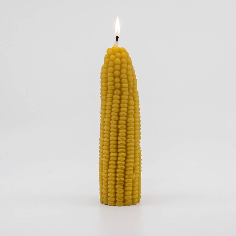 A lit pillar candle shaped like a corn cob. 