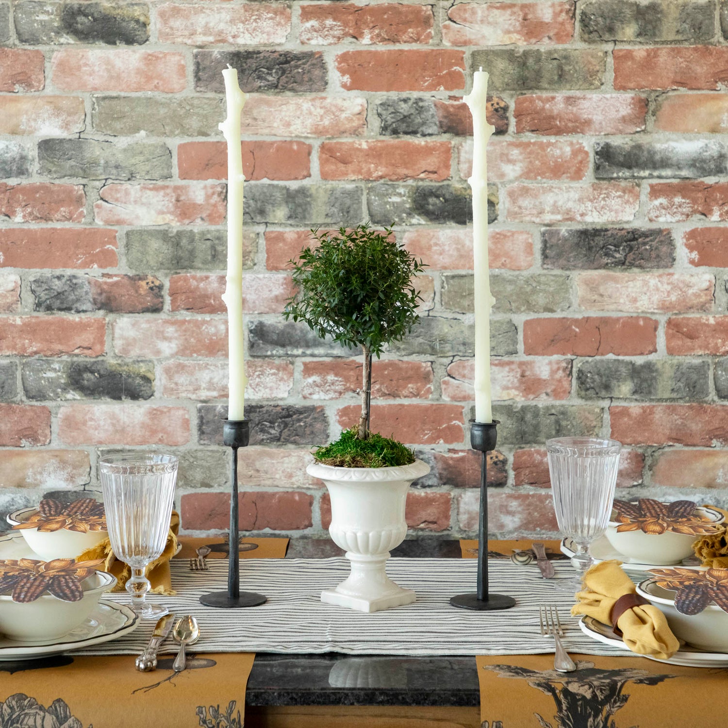 A Stick Candles set and a group of candles on top of a textured brick wall.