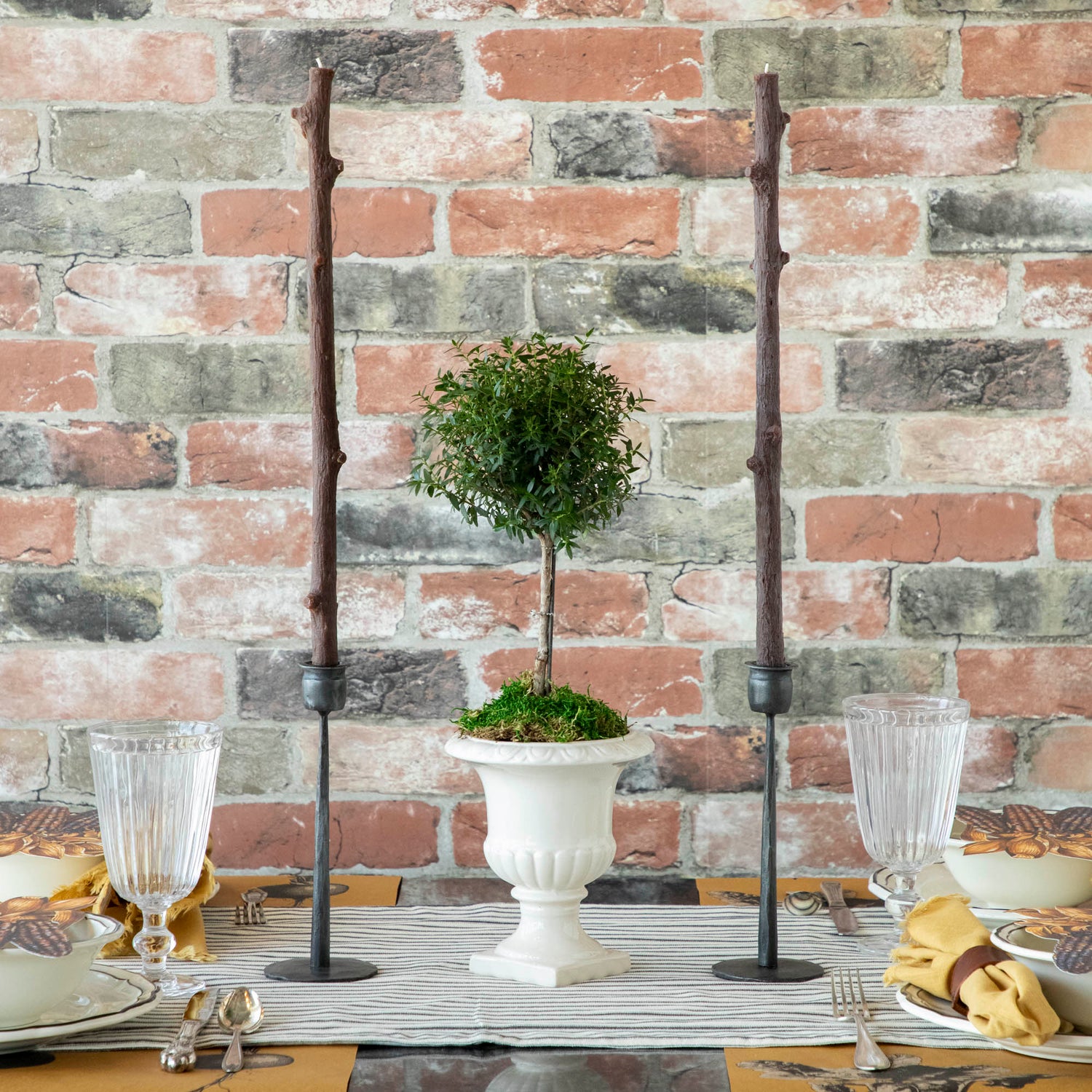 A Stick Candles set and a group of candles on top of a textured brick wall.