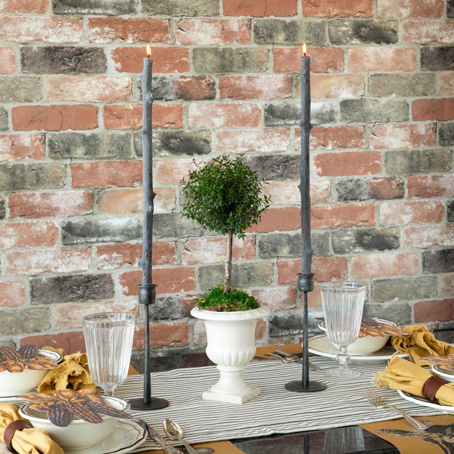 A Stick Candles set and a group of candles on top of a textured brick wall.