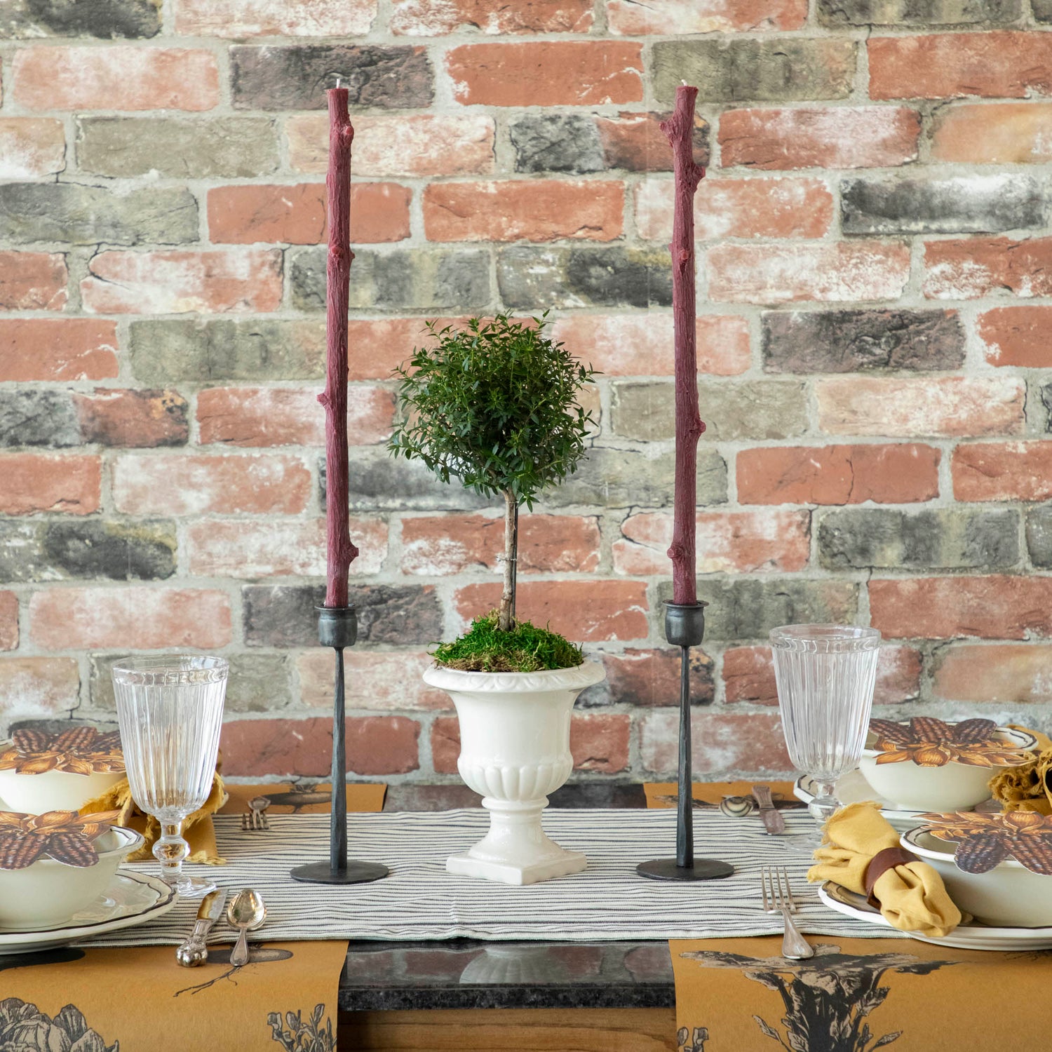 A Stick Candles set and a group of candles on top of a textured brick wall.