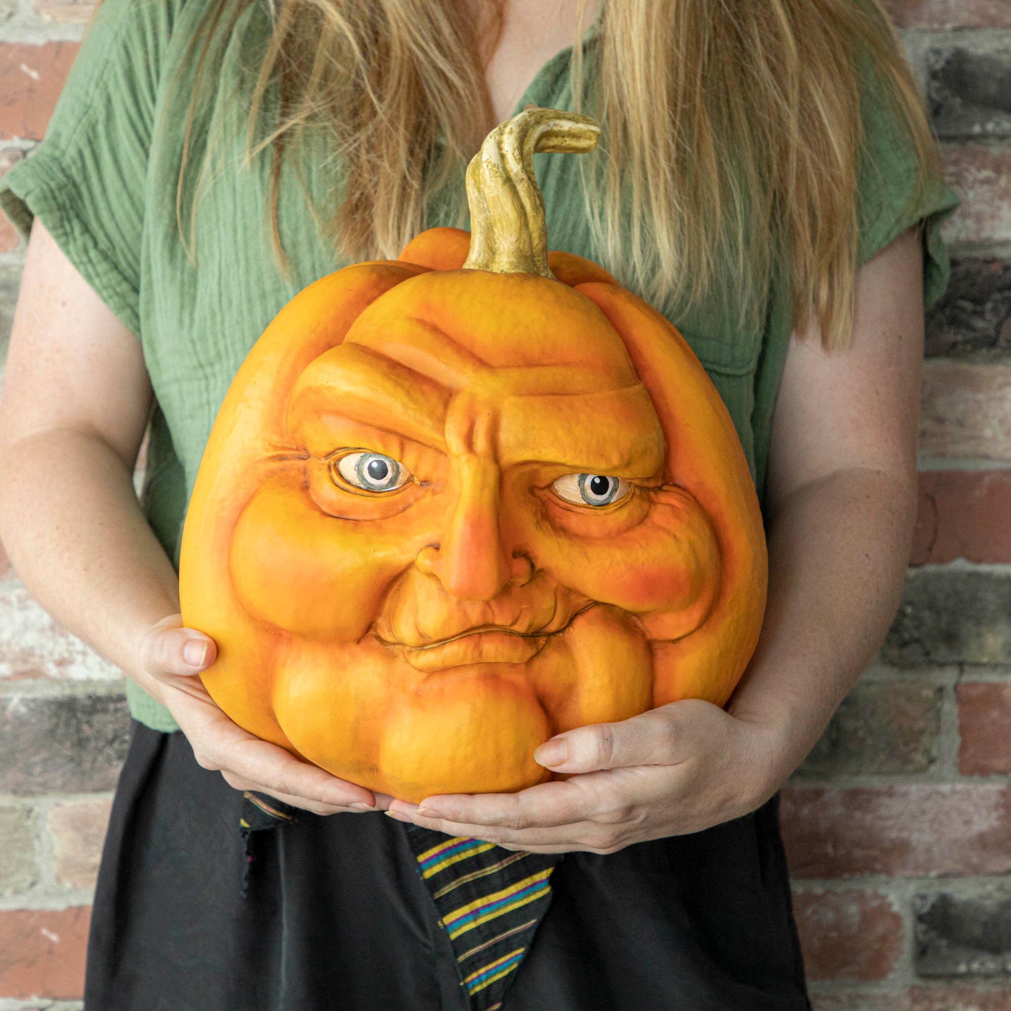 A person holding a resin pumpkin with a smirking face on it.