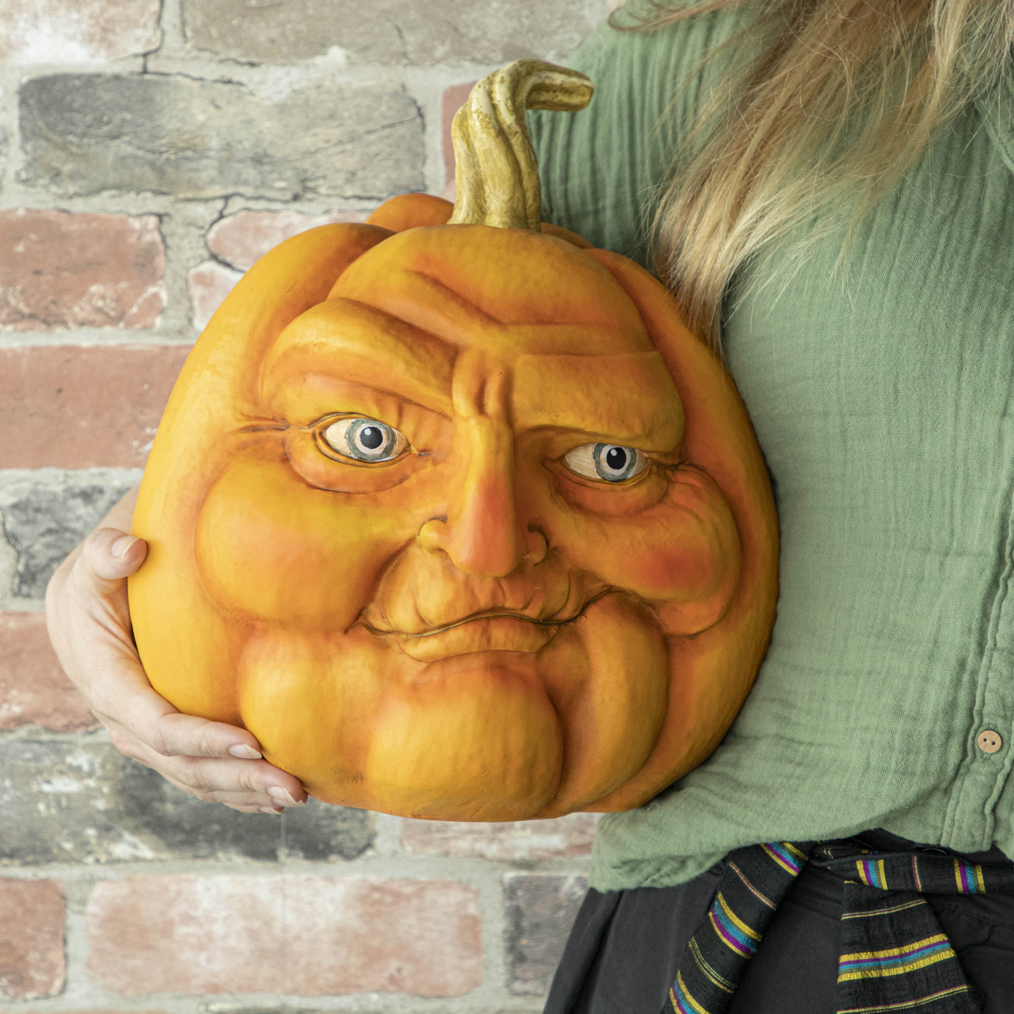 A person holding a resin pumpkin with a smirk on it.