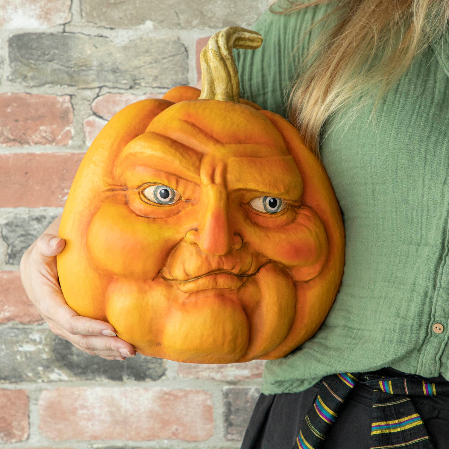 A person holding a resin pumpkin with a smirk on it. 