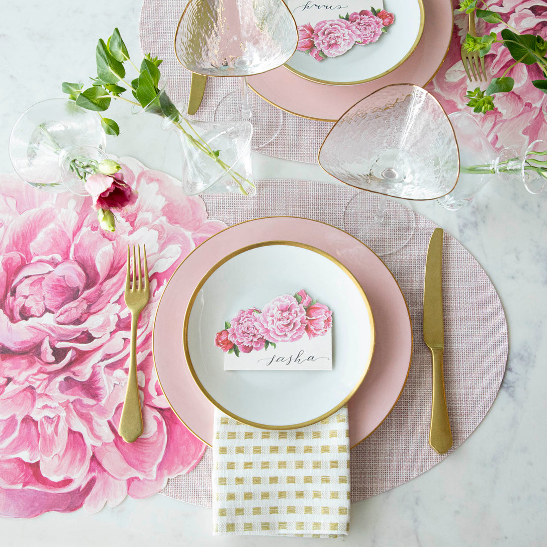 Elegant table setting with a floral theme, featuring pink and white dishes, gold cutlery, Chilewich Blush Mini Basketweave Mats, and personalized name card.