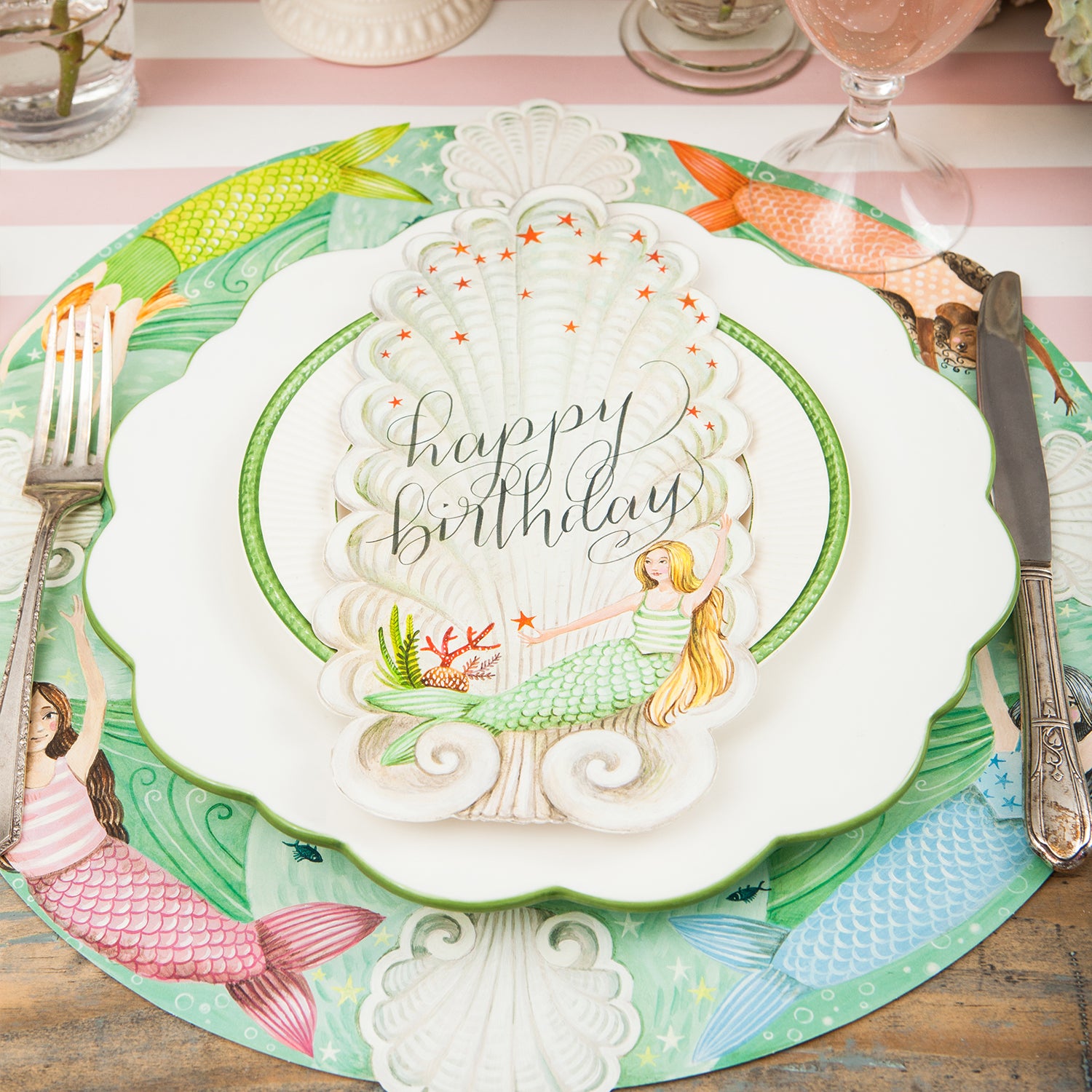 A mermaid-themed place setting featuring a Mermaid Table Accent with "Happy Birthday" written on it in beautiful script resting on the plate.