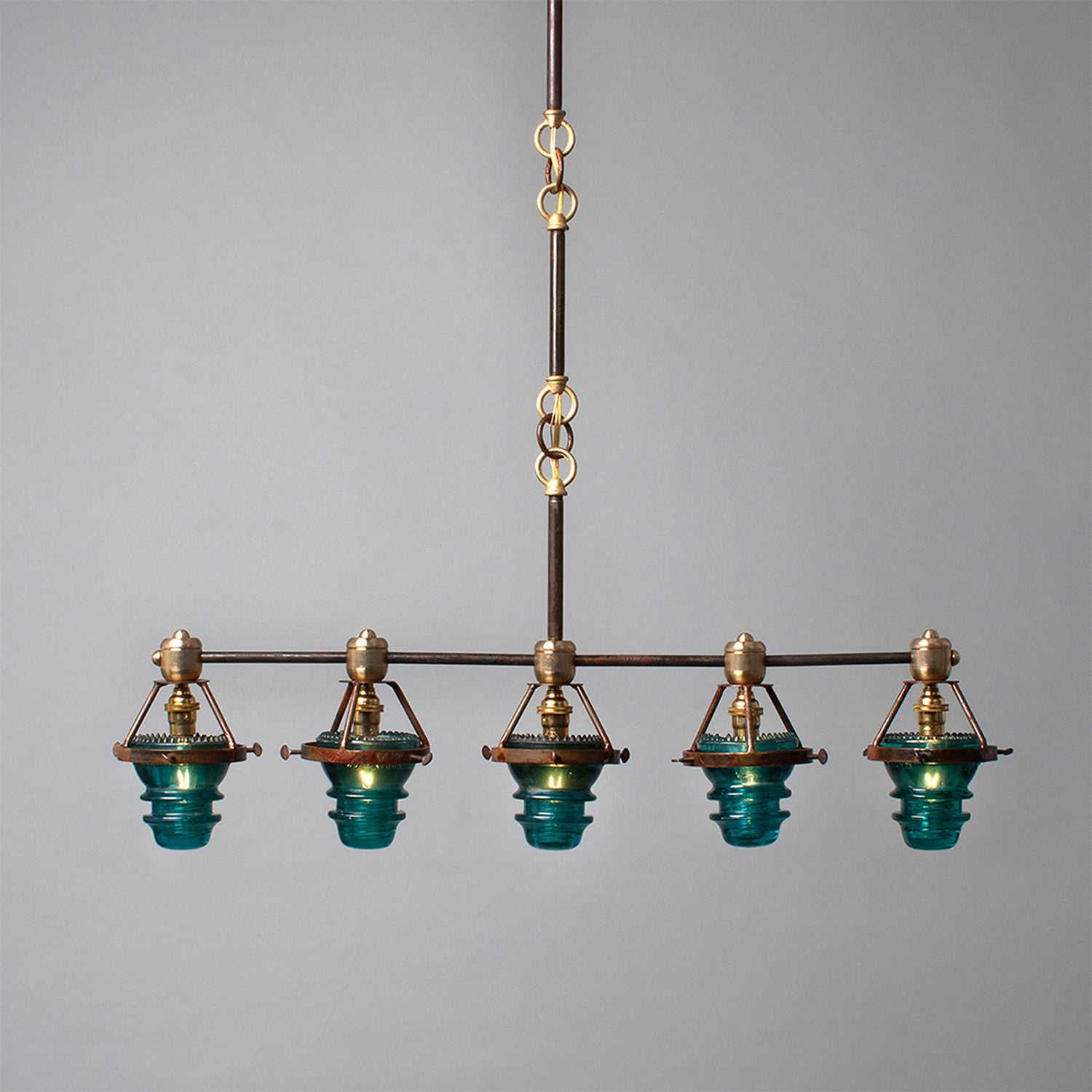 A Telegraph Pendant Lighting with four glass shades and antique insulators hanging from a brass frame. (Brand Name: Hester & Cook)
