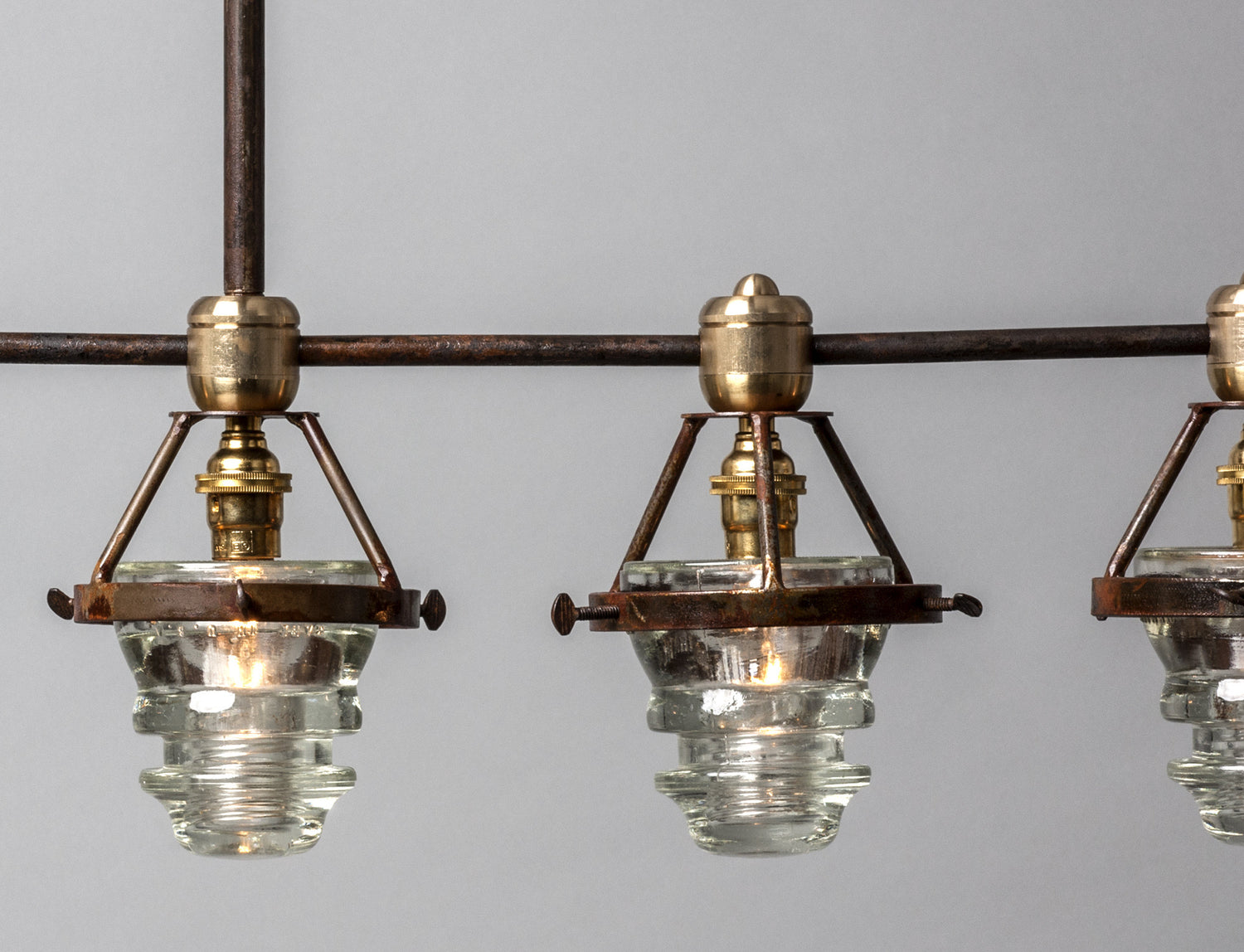 A Telegraph Pendant Lighting with four glass shades and antique insulators hanging from a brass frame. (Brand Name: Hester & Cook)