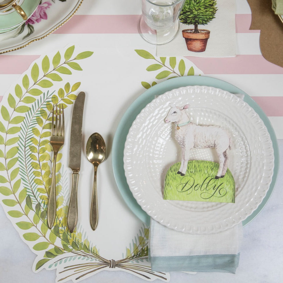 A table setting with a Little Lamb Place Card by Hester & Cook on it, adorned with an Easter Garden Story theme.