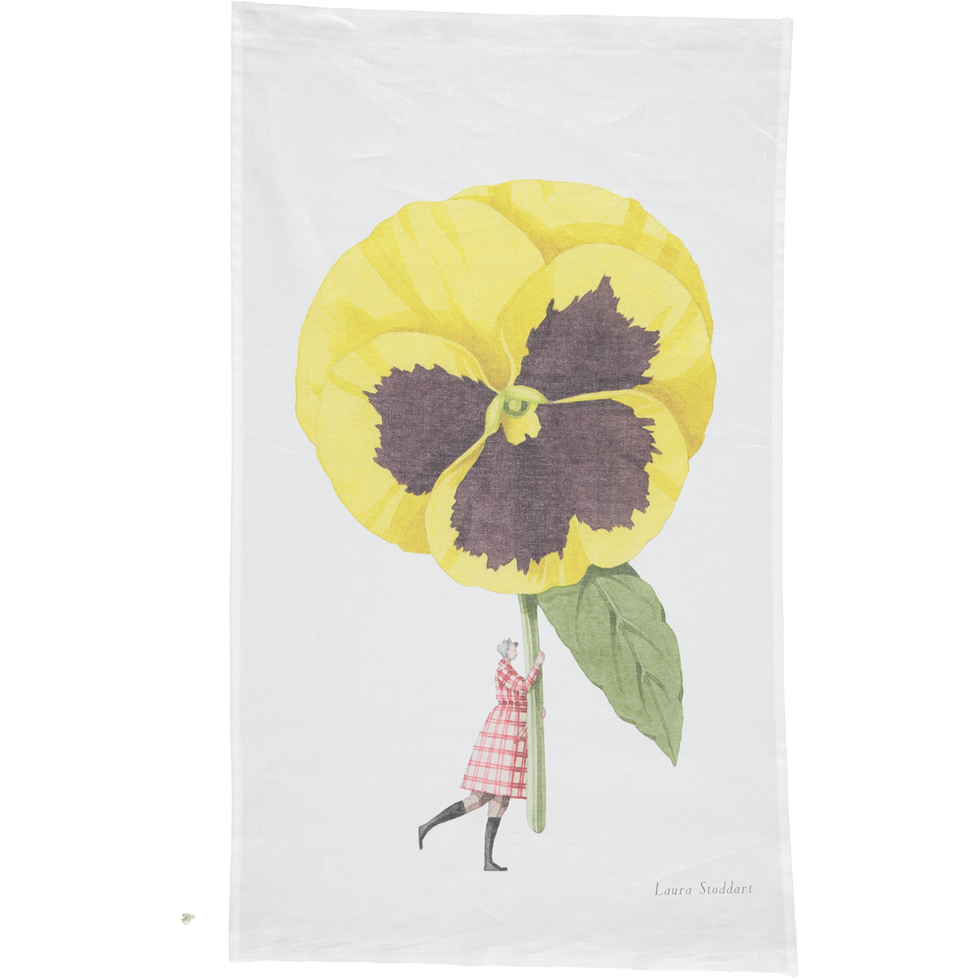 A white tea towel featuring a whimsical illustration of a small woman holding a gigantic yelllow pansy by the stem. Art by Laura Stoddart.