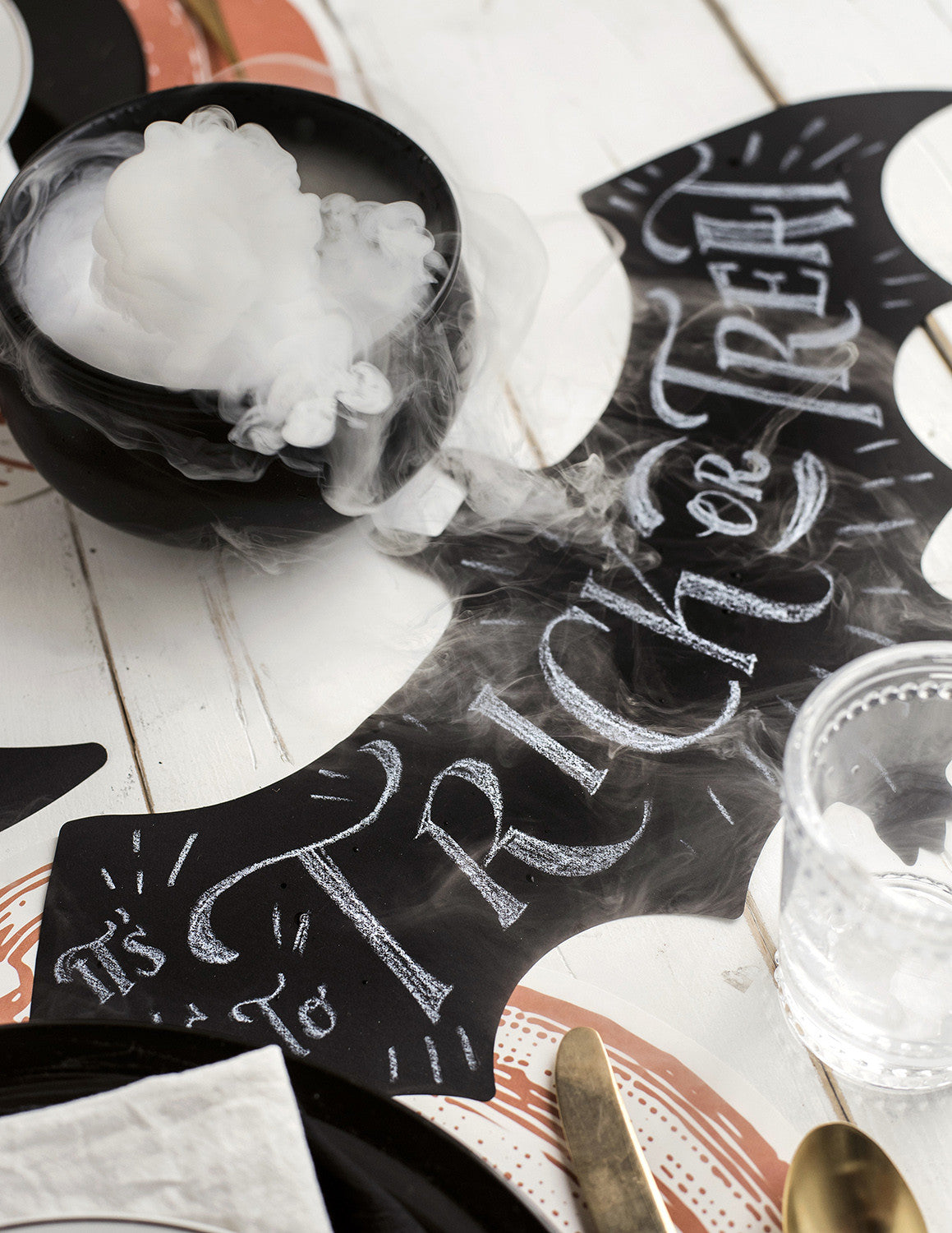 The Die-cut Bat Placemat on a spooky Halloween table setting, with "Trick or Treat" hand-written on it in white chalk.