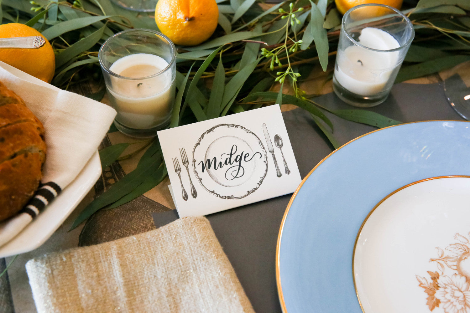 Close-up of a Perfect Setting Place Card labeled "Midge" standing in an elegant place setting.