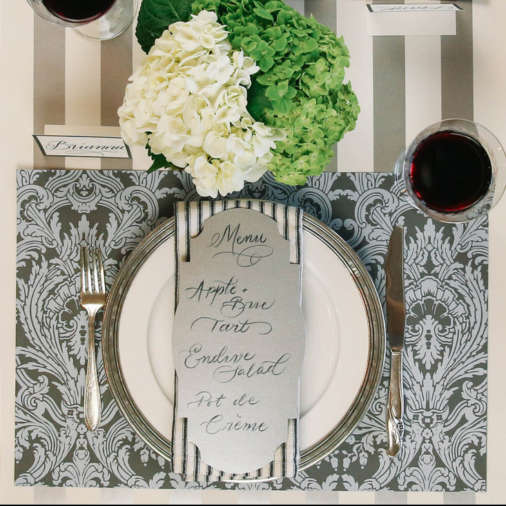 Top-down view of an elegant place setting featuring a Silver Frame Table Accent resting on the plate with a menu written in beautiful script.