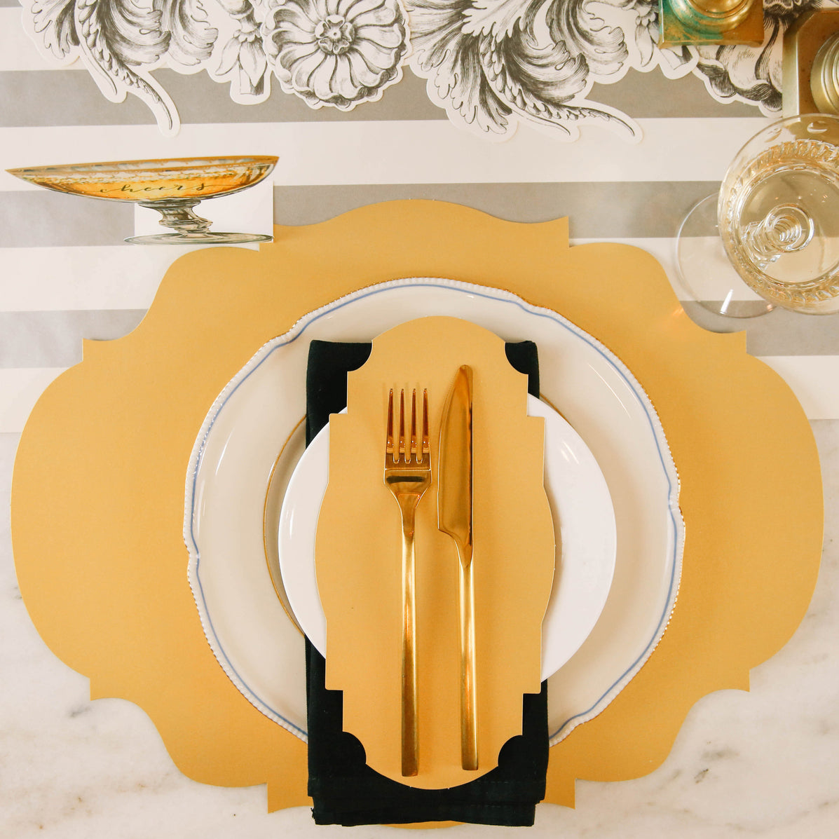 An elegant place setting featuring a Gold Frame Table Accent resting on the plate with the fork and knife on top.