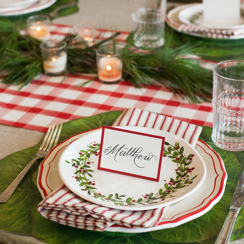 A special Christmas table setting with a Hester & Cook Red Frame Place Card and a red and white checkered tablecloth for guests.