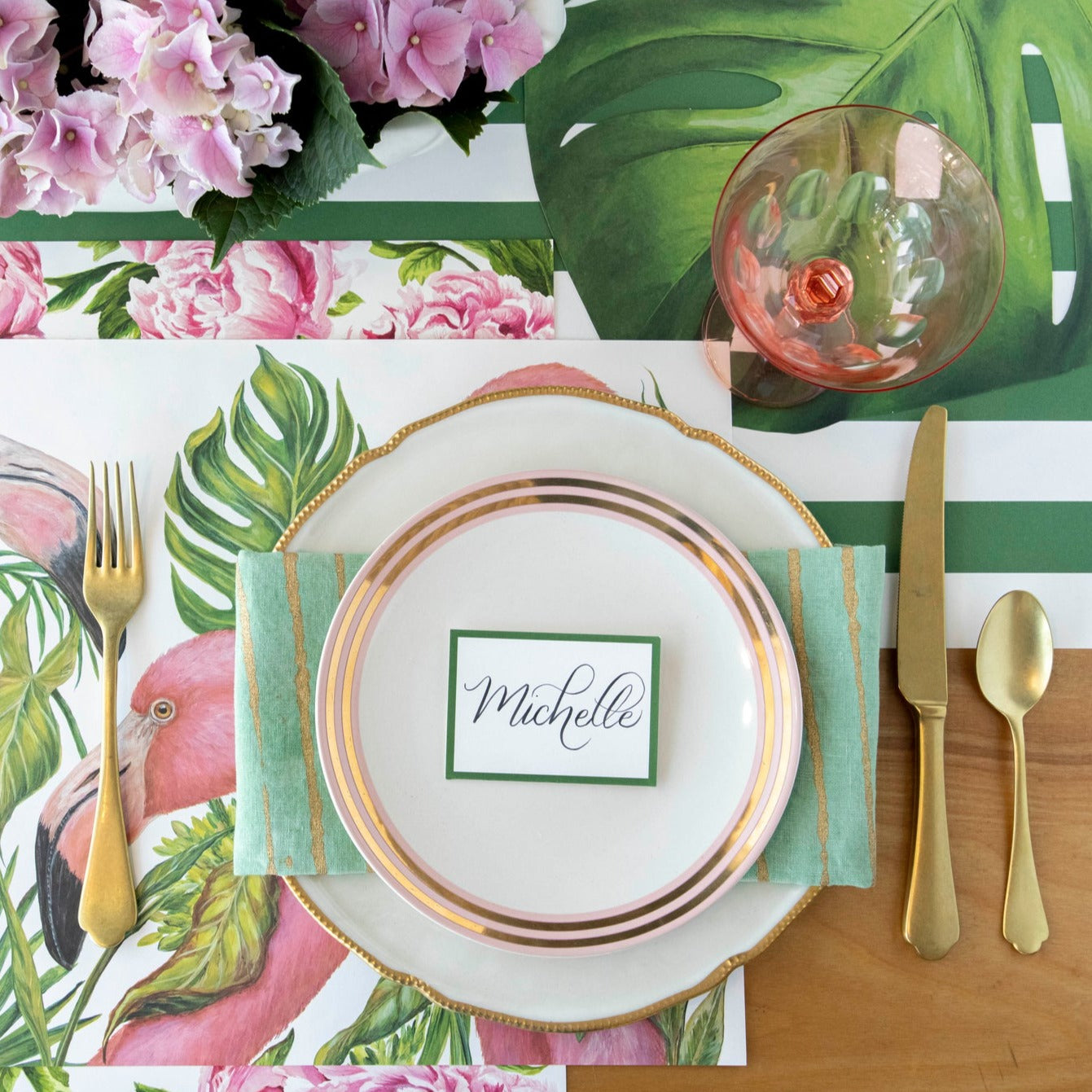 A table setting with an elegant touch of the Die-cut Monstera Placemat from Hester & Cook, adorned with flamingos and flowers.