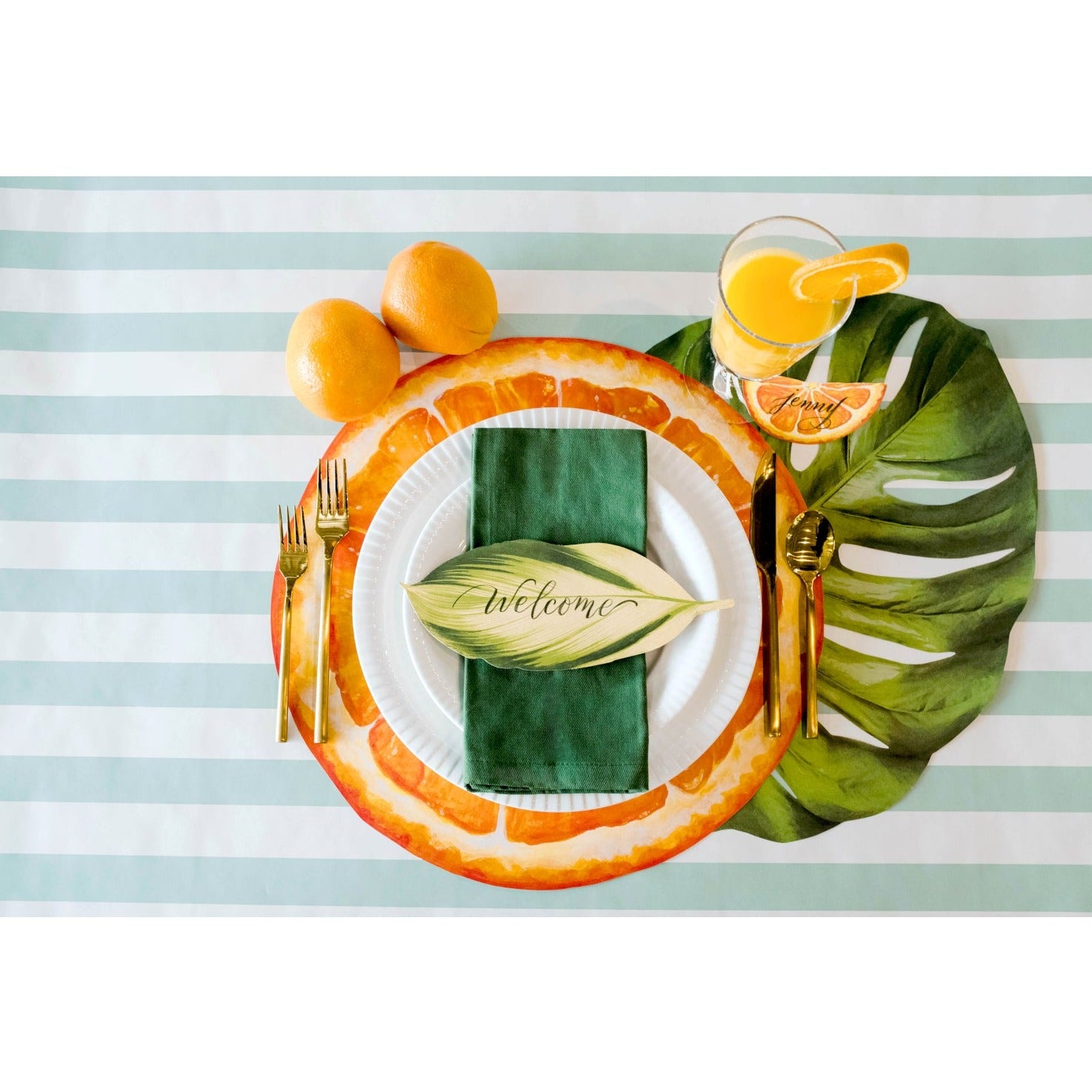 An elegant table setting with oranges, lemons and limes on a striped tablecloth, adorned with Die-cut Monstera Placemat by Hester & Cook.