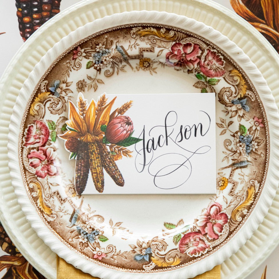 Close-up of an elegant Thanksgiving place setting featuring a Gathering Place Card labeled "Jackson" centered on the plate, from above.