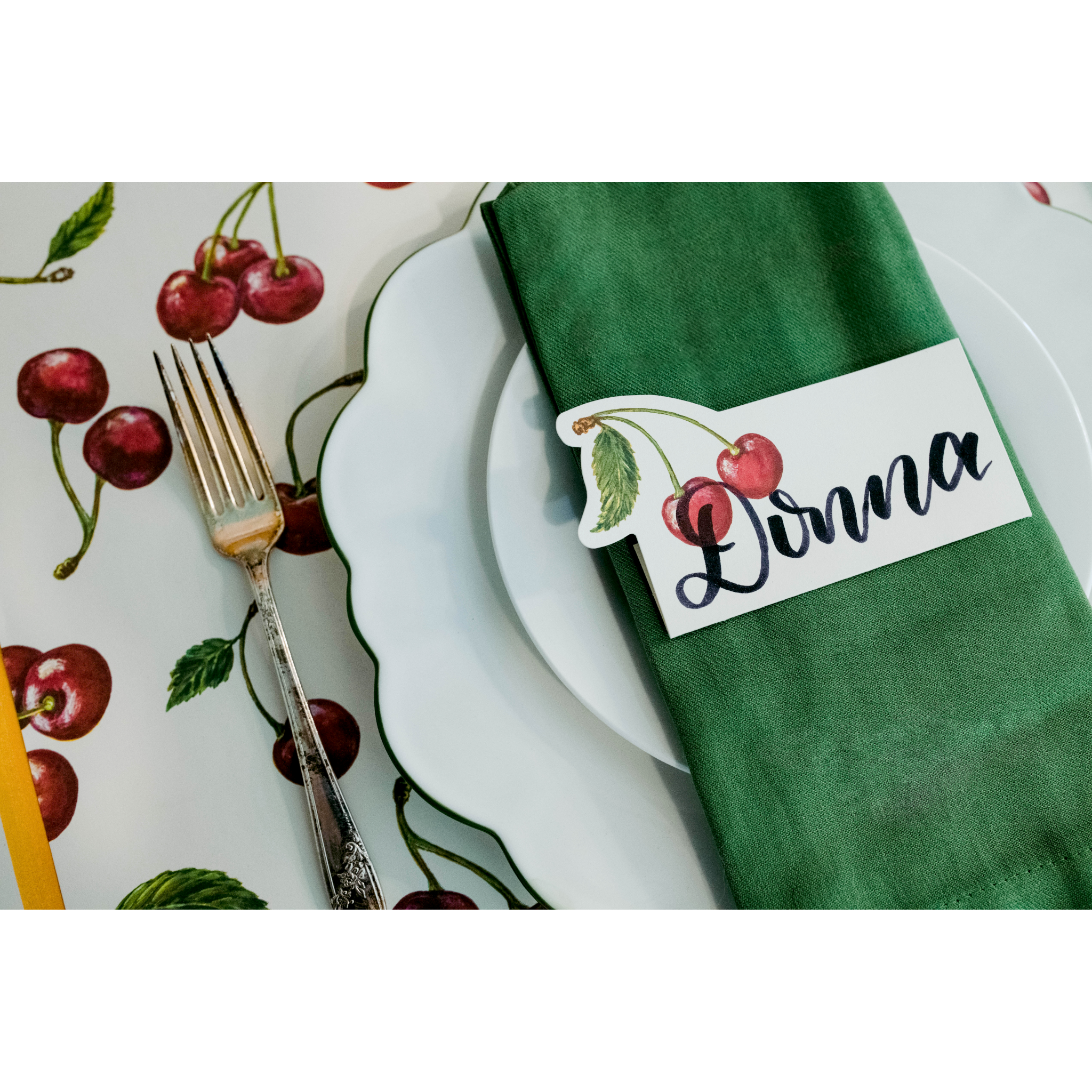 An elegant place setting featuring a Cherries Place Card reading "Donna" laying flat on the napkin over the plate.