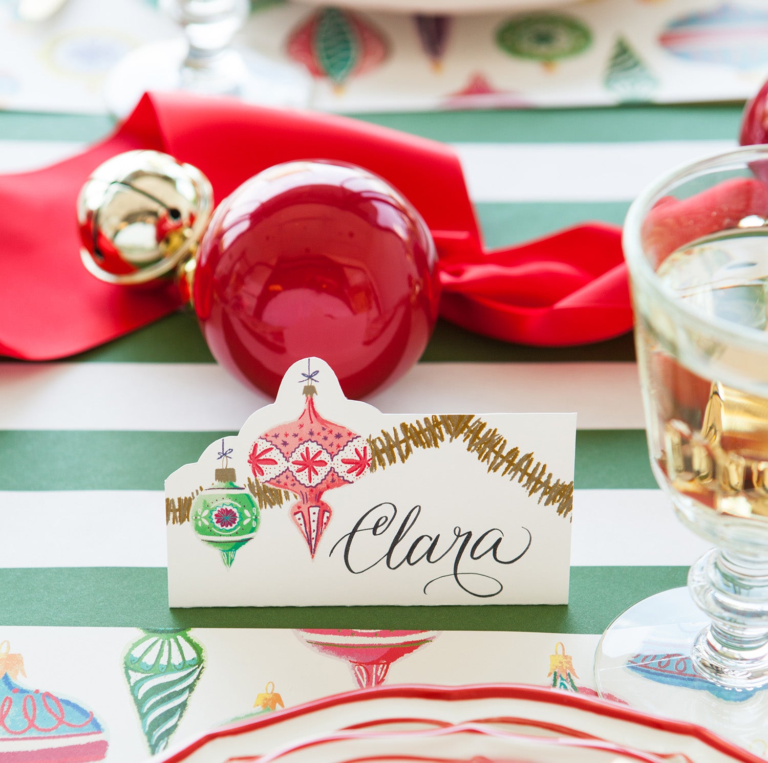Close-up of an Ornaments Place Card labeled "Clara" in beautiful script, standing behind the plate of a festive holiday place setting.