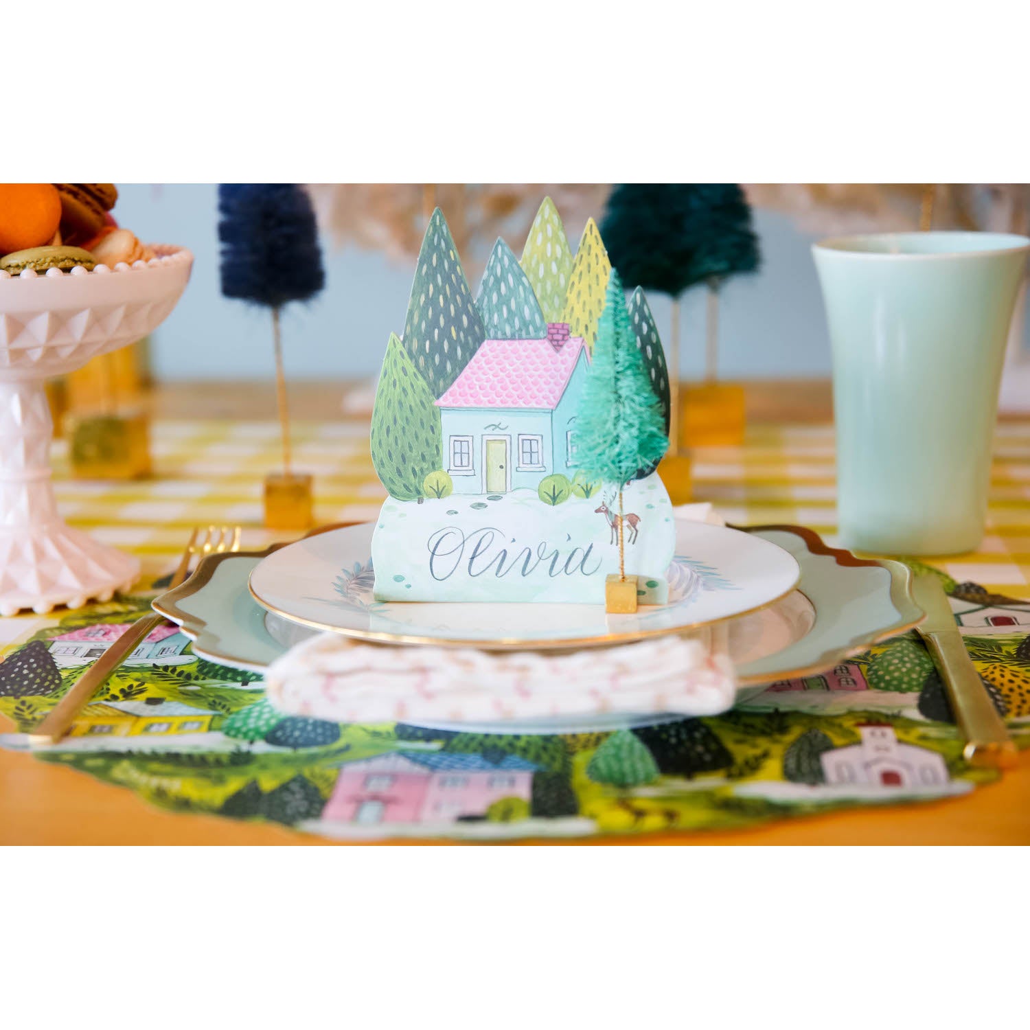 A charming winter-themed place setting featuring a Winter Village Place Card labeled "Olivia" standing on the plate.