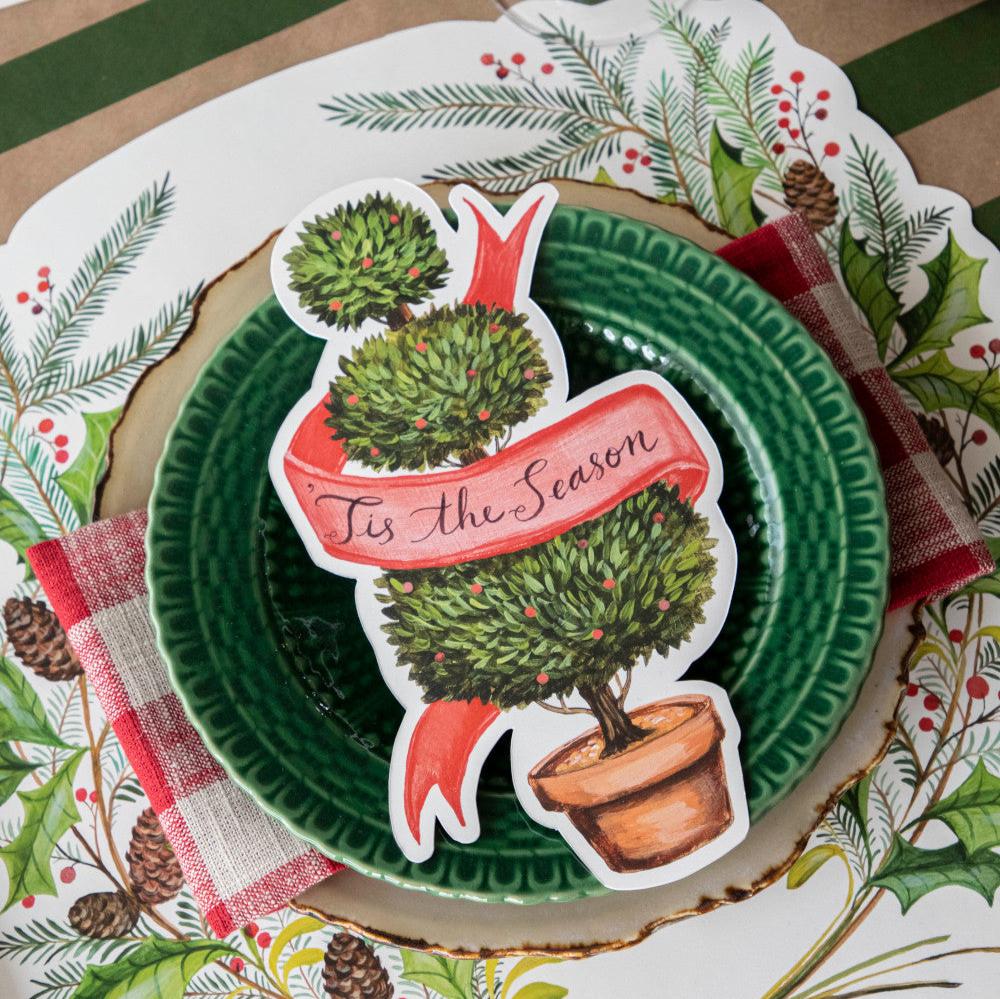 A die-cut illustration of a potted shrub manicured into three balls, with a blank red ribbon twisting around the topiary, creating a space for personalization.