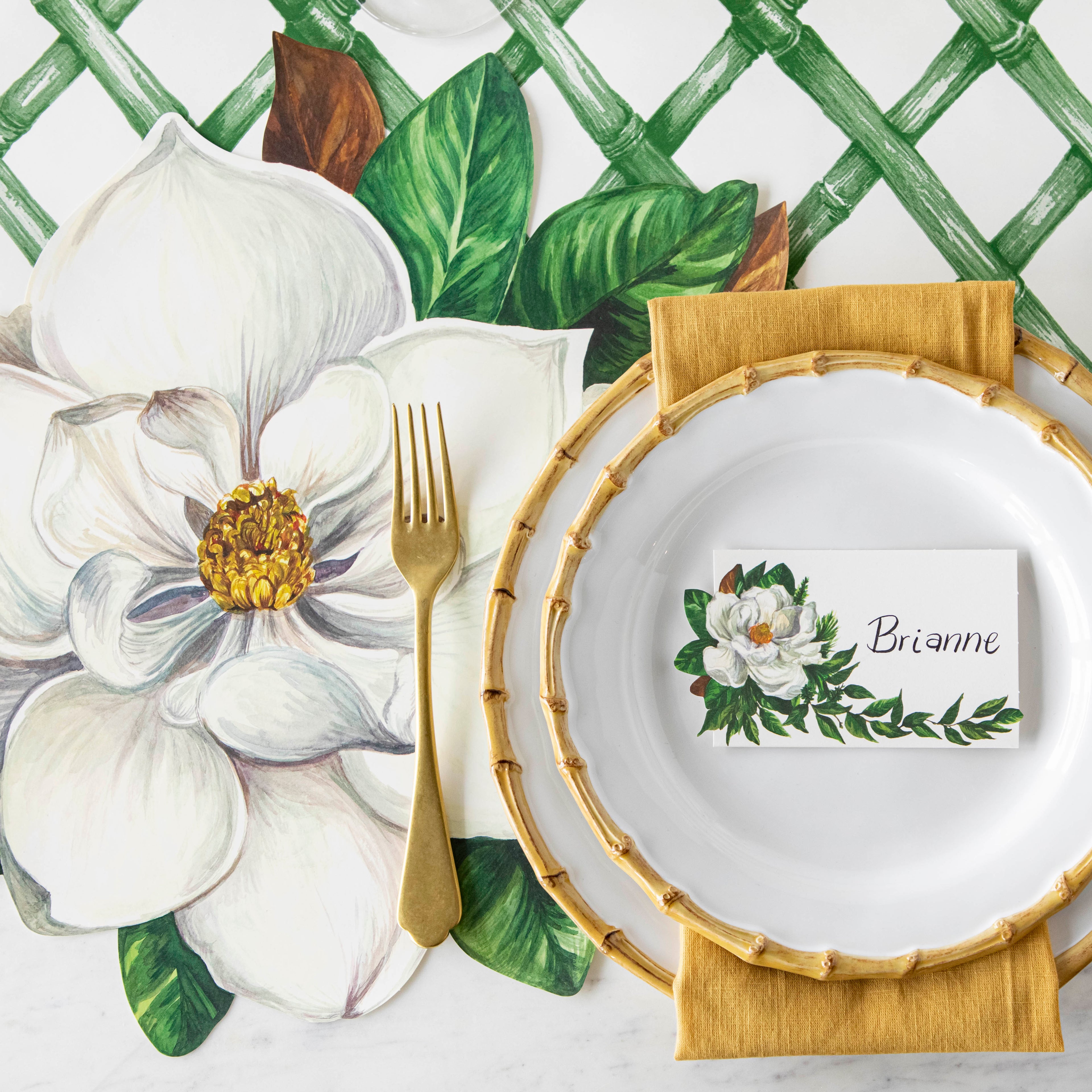Top-down view of an elegant place setting featuring a Magnolia Place Card labeled "Brianne" laying flat on the plate.