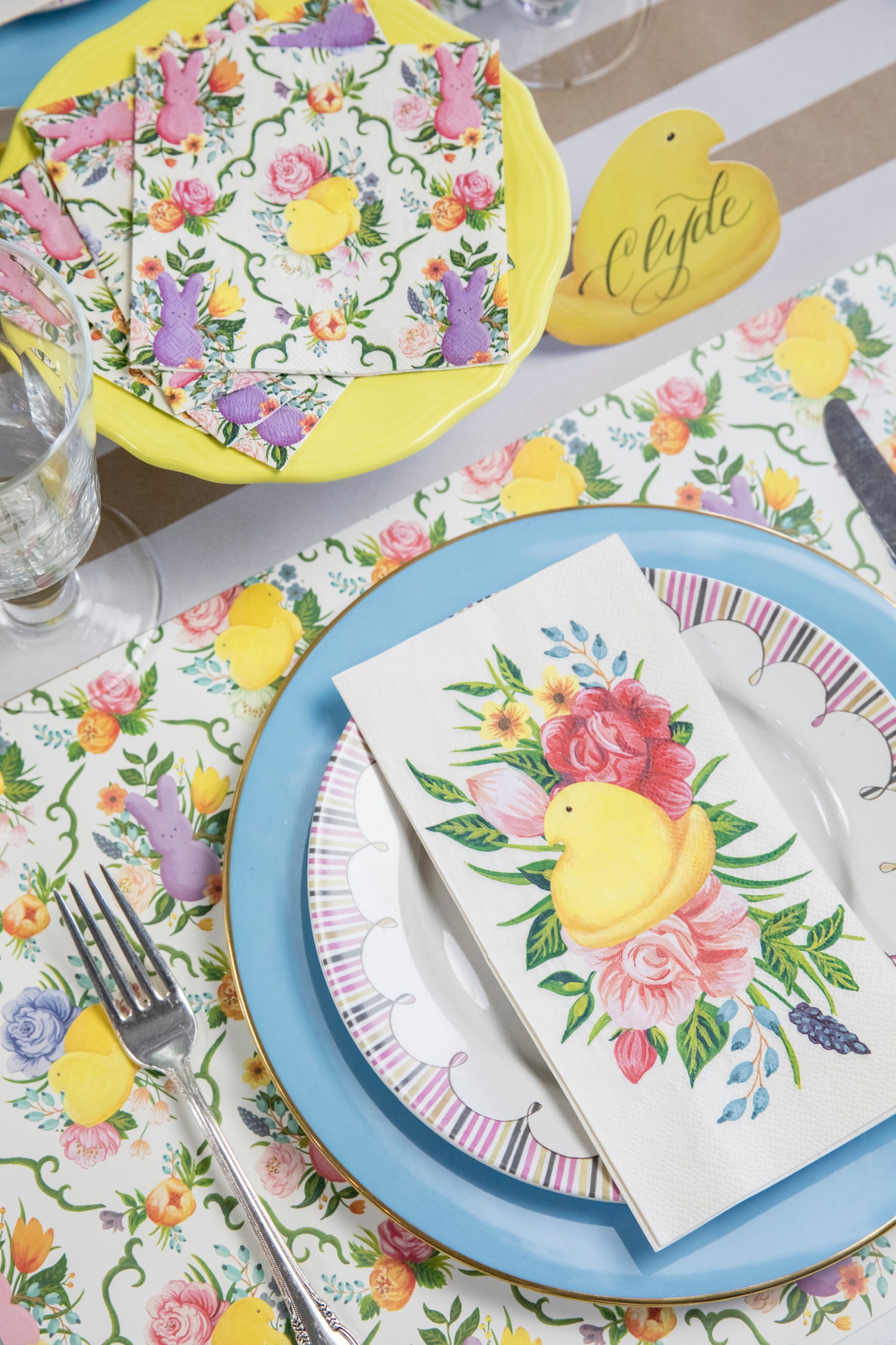 A whimsical Easter table setting featuring a PEEPS® Guest Napkin centered on the plate, and a stack of fanned out PEEPS® Cocktail Napkins on a cake stand.