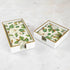 A lacquered wood holder for beverage and guest napkins, featuring a white color with gold trim and a floral pattern napkin inside.