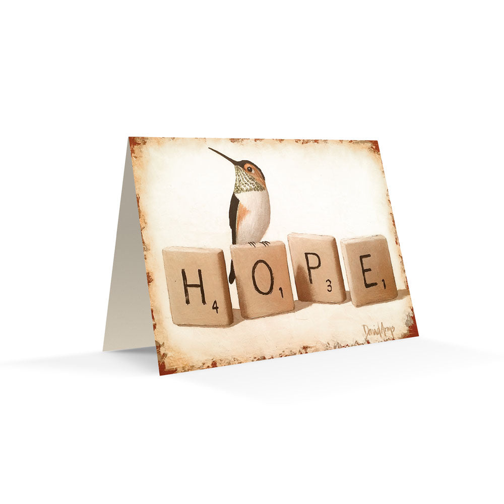 A "Hope" (Scrabble) notecard with a hummingbird illustration and the word "hope" spelled out with letter tiles rests on a woven surface. (David Arms)