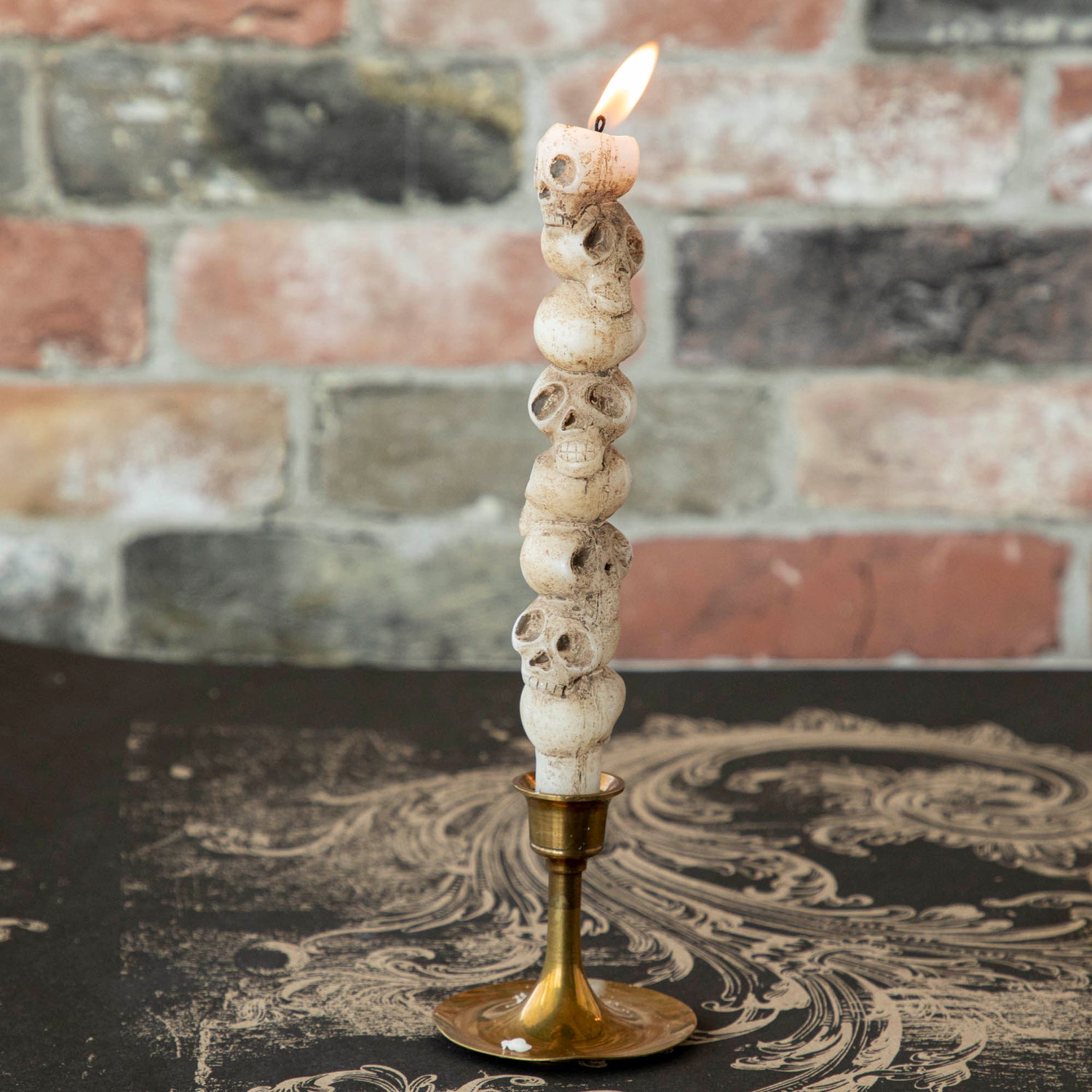 Stacked skull shaped taper candle in a brass candle holder. 