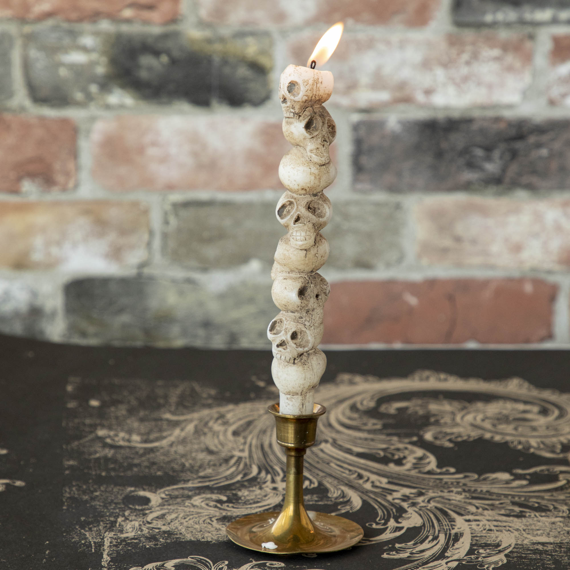 Stacked skull shaped taper candle in a brass candle holder. 