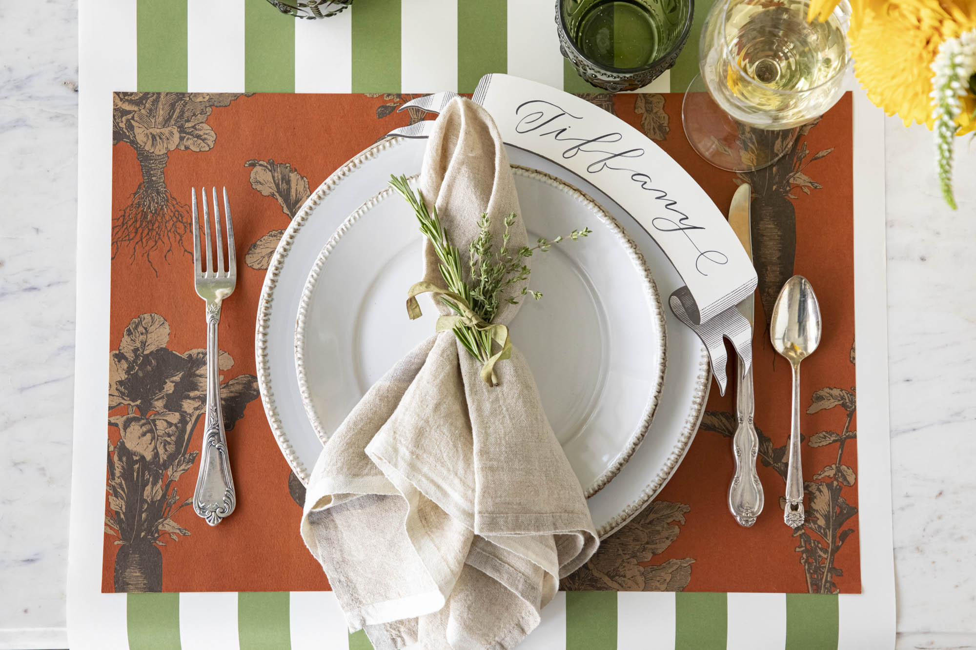 A plate of fresh carrots on a table with a vegetable-themed tablecloth, flanked by cutlery with orange handles.